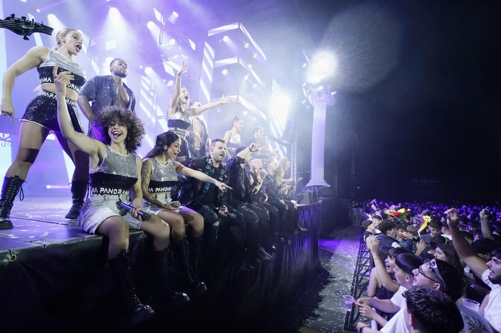 Los cantantes y bailarines y algunos músicos se asoman al borde del escenario.