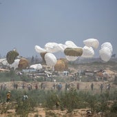 Decenas de palestinos corren hacia el lugar donde aterrizan paquetes de ayuda humanitaria en paracaídas en el centro de Gaza.