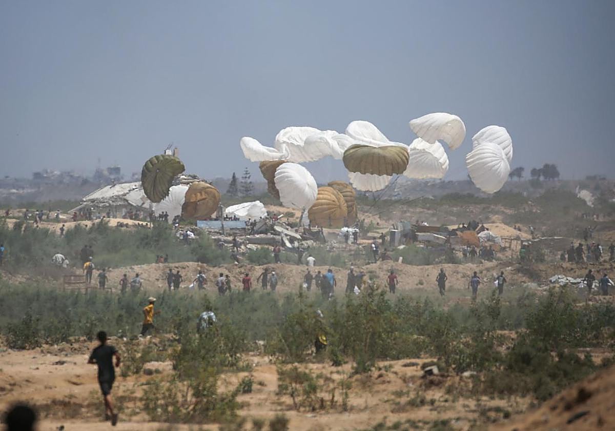 Decenas de palestinos corren hacia el lugar donde aterrizan paquetes de ayuda humanitaria en paracaídas en el centro de Gaza.