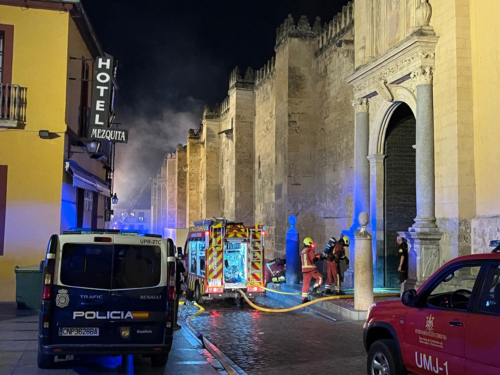 Imagen secundaria 1 - En la imagen superior, un bombero que participaba en las tareas de extinción desde una escala exterior; debajo, aceso al interior de la Mezquita-Catedral de Córdoba por parte de los servicios de emergencias; por último, las llamas y un denso humo negro fueron la señal de alarma para que varios vecinos alertasen a las autoridades del incendio desatado este viernes.