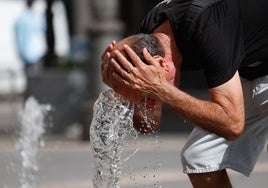 Una hombre se refresca en un surtidor para paliar el calor sofocante.