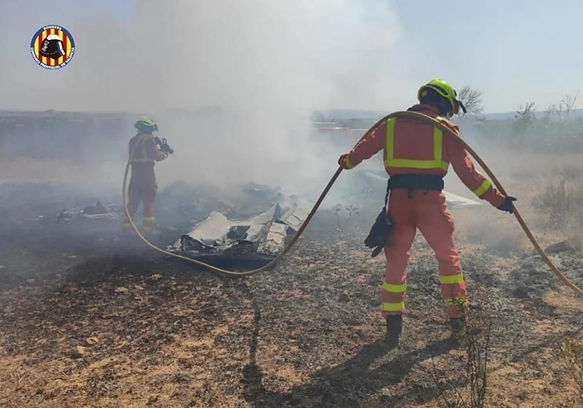 Dos bomberos trabajan para apagar el fuego que ha calcinado la avioneta.