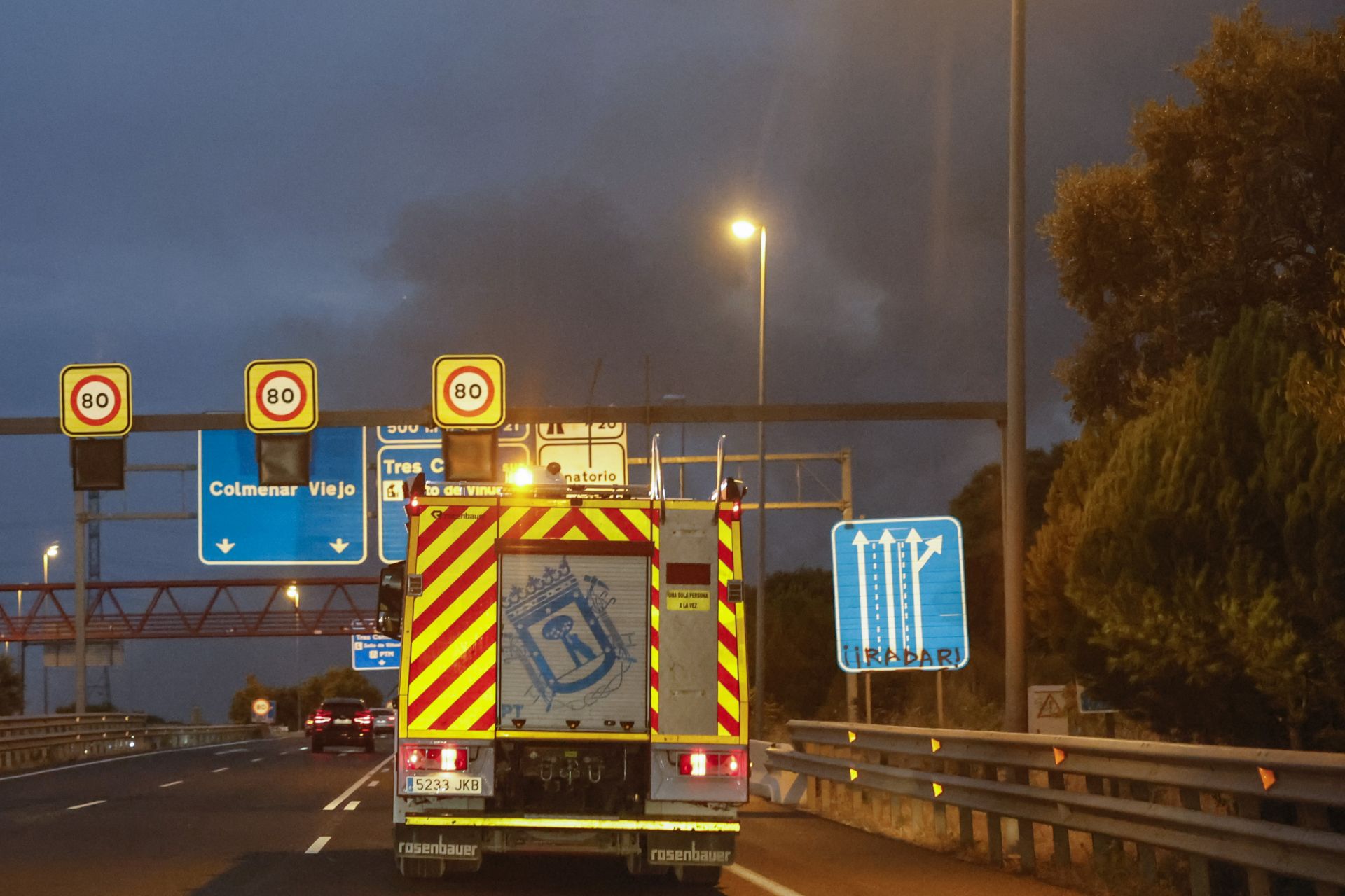 Imagen secundaria 2 - En la imagen superior, acceso a una de las urbanizaciones que ha tenido que ser desalojada por su cercanía al incendio desatado este lunes; debajo, avance de las llamas en una zona de vegetación y pastos; por último, una dotación de Bomberos de Madrid en la carretera M-607 de Colmenar Viejo camino de ayudar en la extinción del fuego en Tres Cantos.