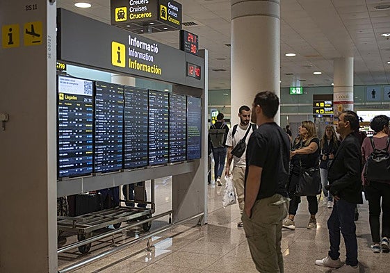 Varias personas observan un panel de llegadas en el aeropuerto de Barcelona