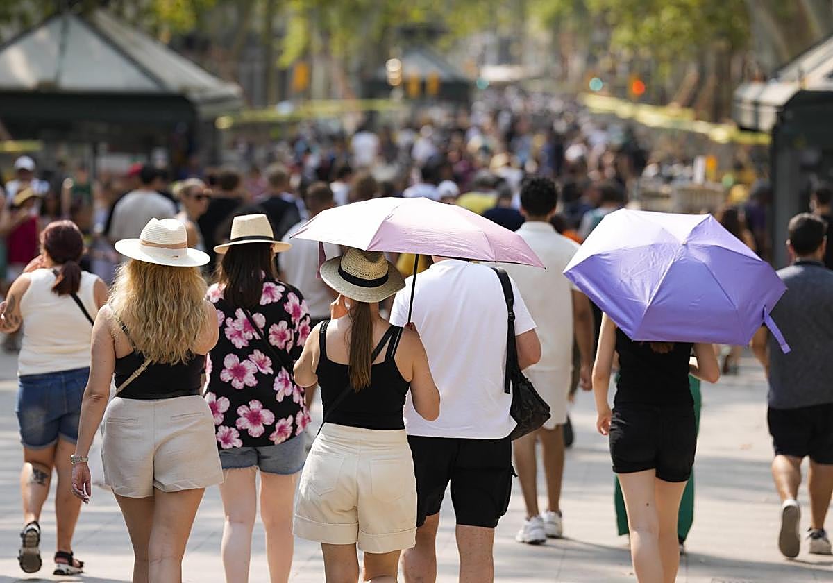 Un grupo de turistas se protege del sol con sombrillas este domingo en Barcelona