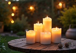 Acogedor jardín al aire libre con cinco velas de citronela encendidas sobre una mesa rústica de madera, rodeada de vegetación, creando un ambiente cálido y tranquilo para noches relajantes.