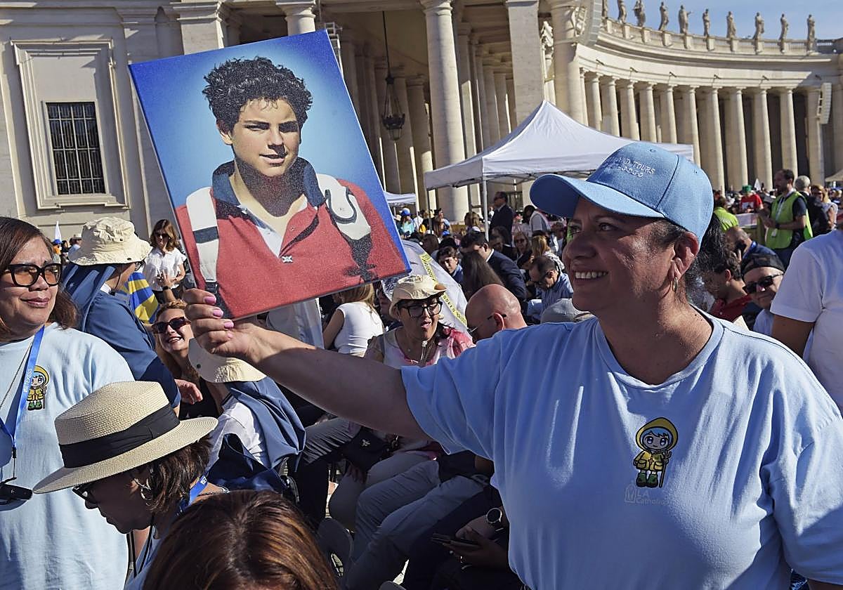 Una mujer posa junto a una imagen de Carlo Acutis, en la Plaza de San Pedro del Vaticano.