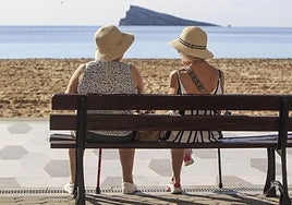Dos mujeres disfrutan del buen tiempo sentadas ante la playa de Levante de Benidorm.