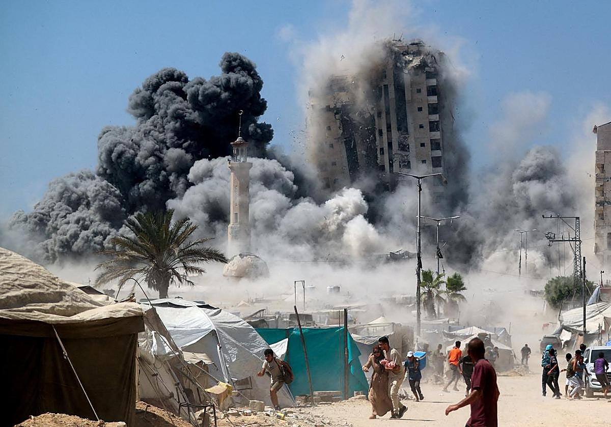 Un grupo de palestinos huye mientras se derrumba una torre de edificios en Ciudad de Gaza al ser alcanzada por un bombardeo israelí.