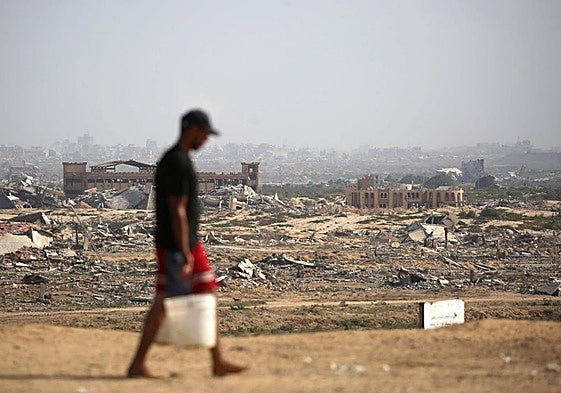 Un joven palestino acarrea agua delante de un paisaje ruinoso de casas devastadas después de que se suspendiera la ocupación militar.