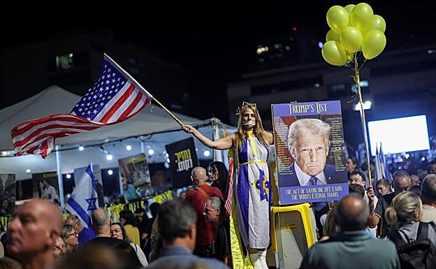 Una mujer ondea una bandera de EE UU y exhibe un retrato de Trump en la Plaza de los Rehenes.