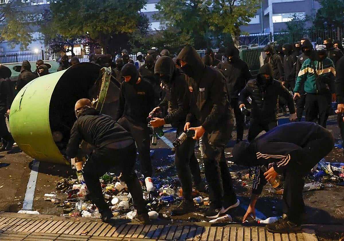 Jóvenes encapuchados recogen botellas de un cubo de basura.