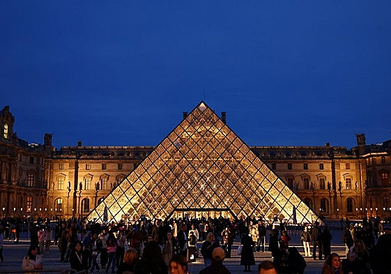 La gente camina cerca de la pirámide de cristal del museo del Louvre.
