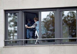 Una empleada del hogar trabaja limpiando una ventana.