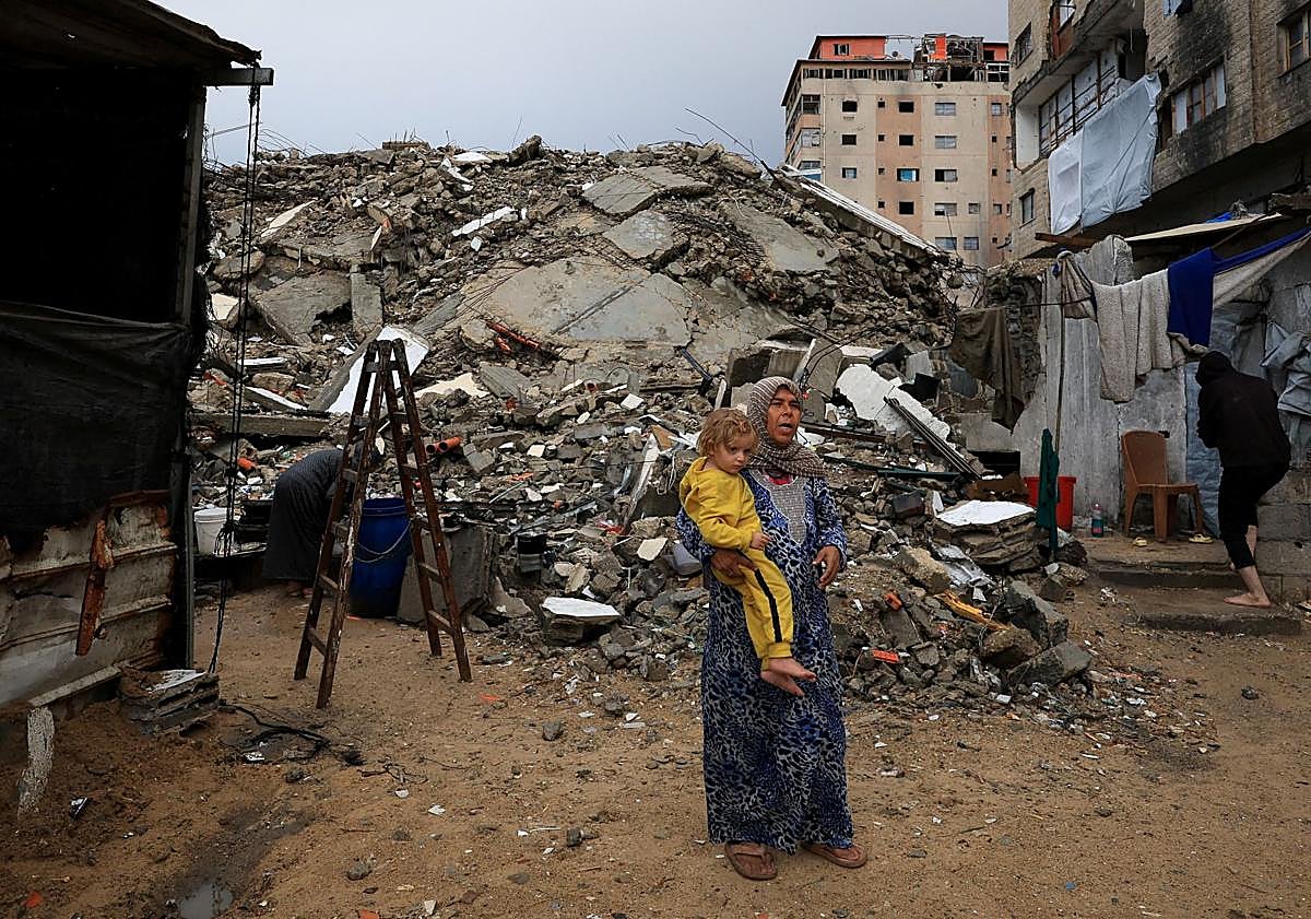 Imagen principal - Una mujer con un crío en brazos entre los restos de la guerra en Ciudad de Gaza; edificios reducidos a escombros en el barrio de Radwan, en el norte de la Franja; un niño trata de empujar el agua tras las lluvias sobre el enclave. 