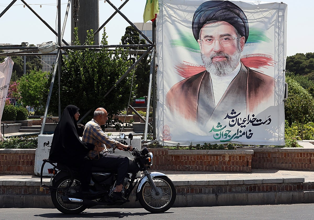 Dos ciudadanos iraníes circulan frente a un retrato de Mojtaba Jamenei.