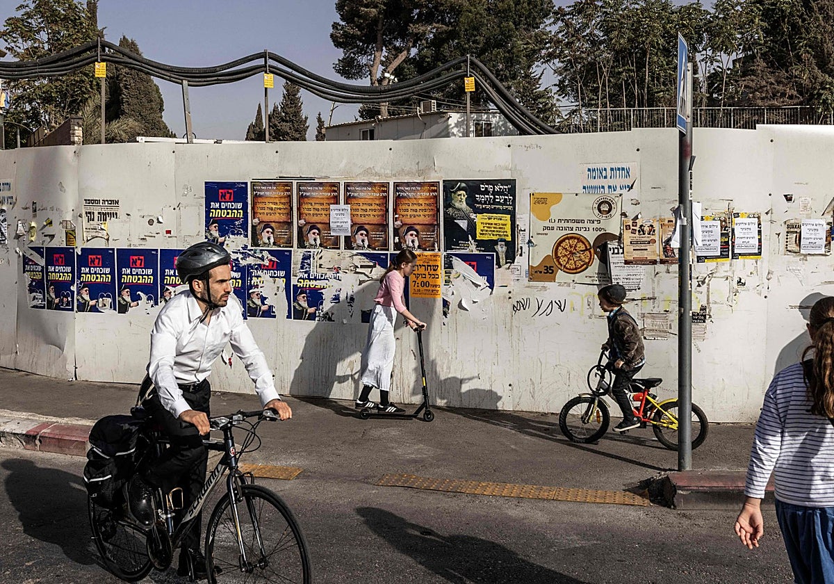 Varias personas pasan por delante de una pared con carteles electorales en Jerusalén.