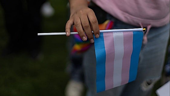 Una persona sostiene una bandera trans.