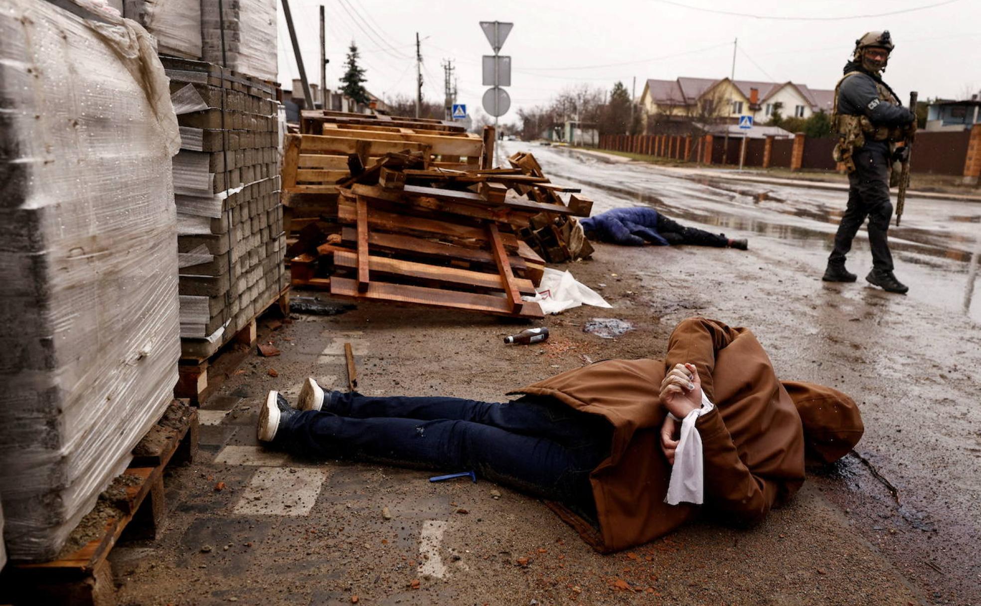 Un paramilitar ucraniano custodia cadáveres de civiles -uno con las manos atadas a la espalda- en una calle de Bucha. 