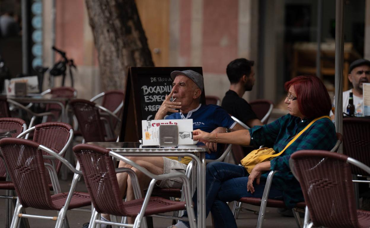 Un hombre fuma sentado en la mesa de una terraza.