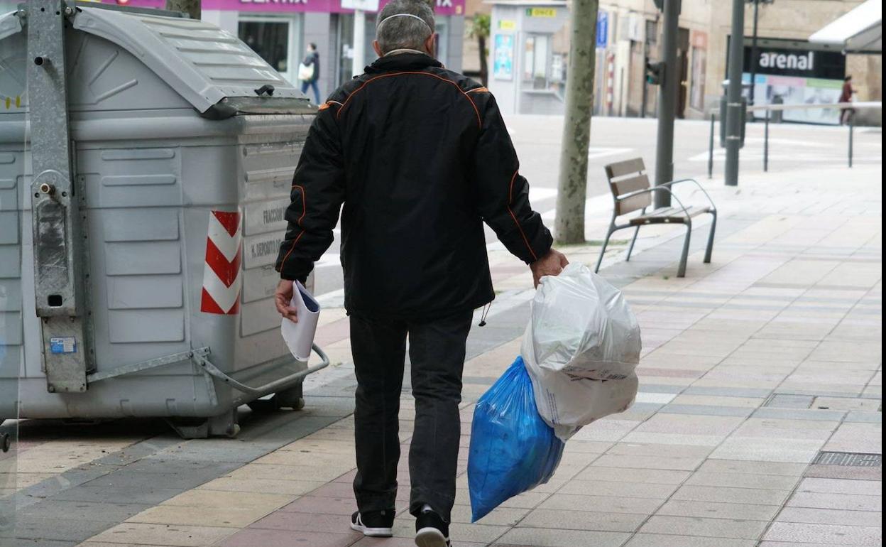 Una persona se dirige con varias bolsas de basura hacia un contenedor. 