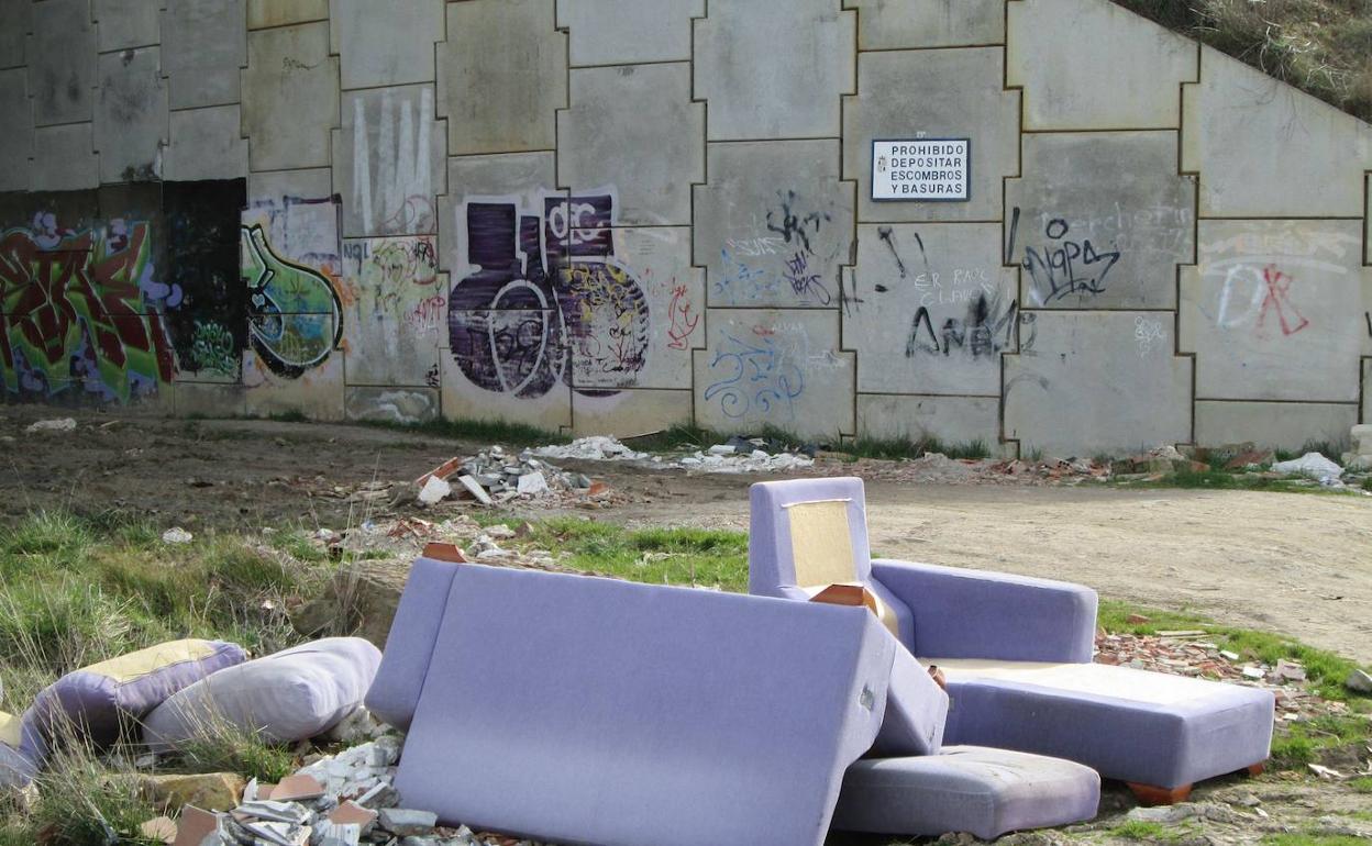 Un sofá y diversos escombros en la entrada a El Zurguén, con el cartel de prohibido depositar basuras al fondo en el muro.