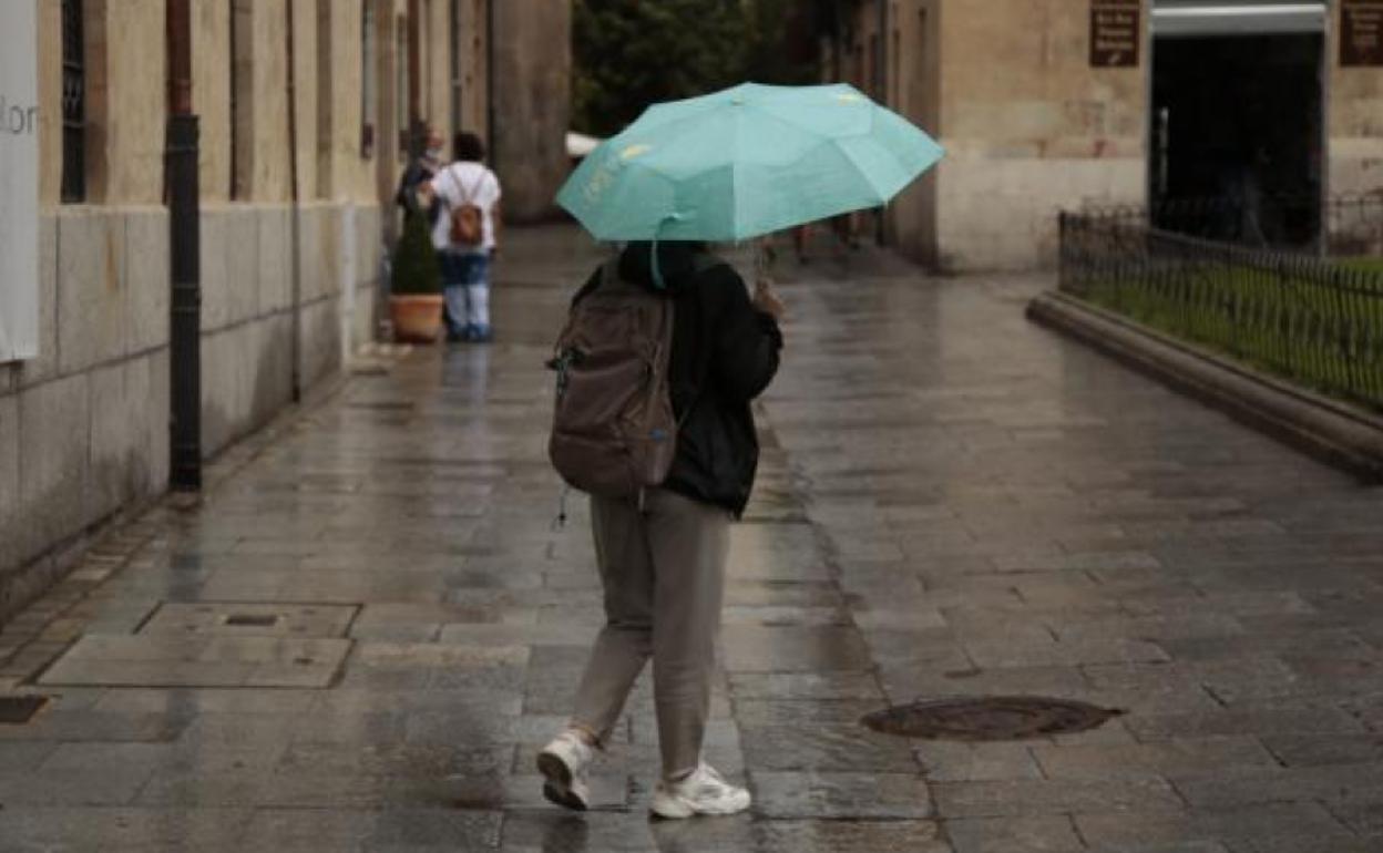 Una persona resguardándose de la lluvia con un paraguas mientras camina por el centro de Salamanca.