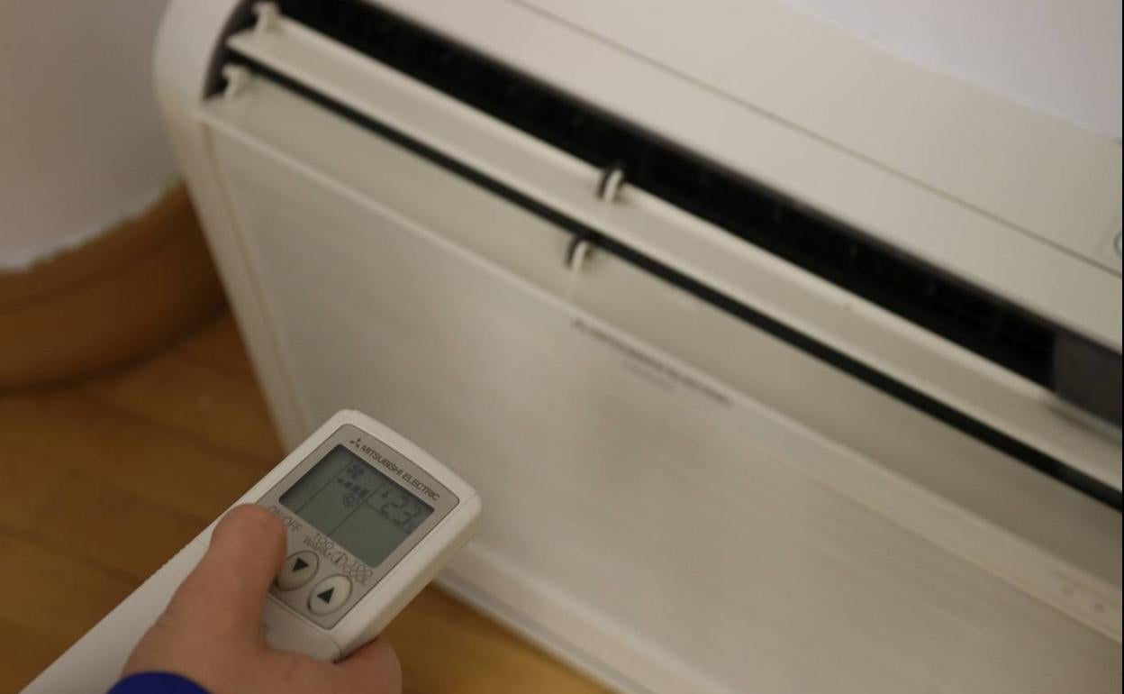 Una persona manipula el mando de un aparato de aire acondicionado.