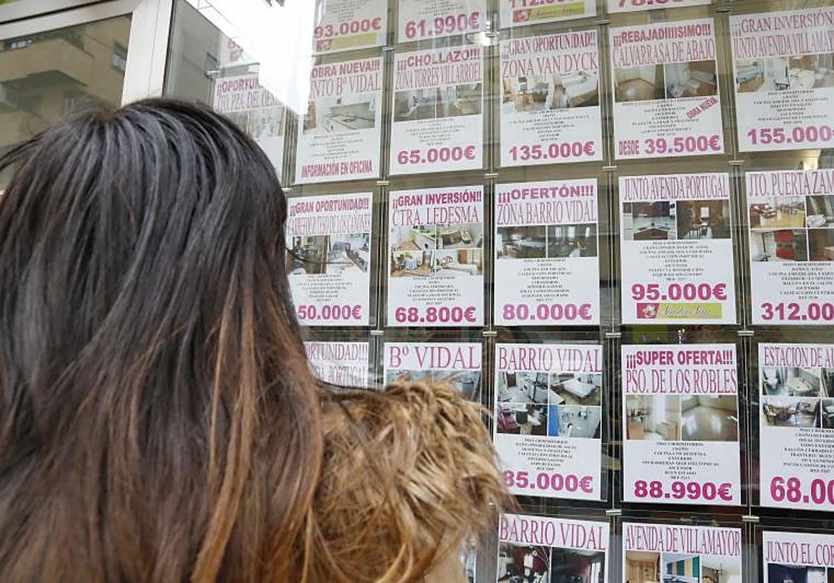 Una mujer observa el escaparte de una inmobiliaria lleno de ofertas de venta de viviendas.
