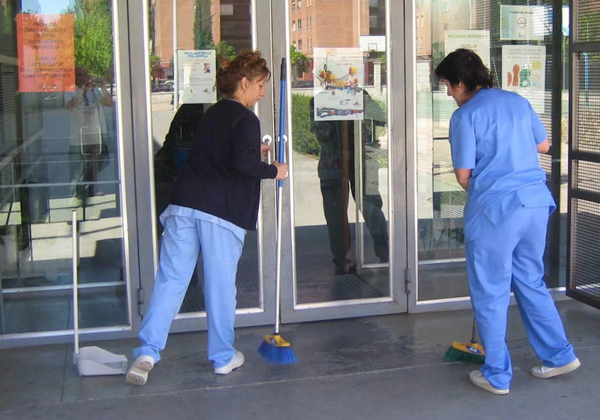 Dos mujeres limpiando en la puerta de un colegio.