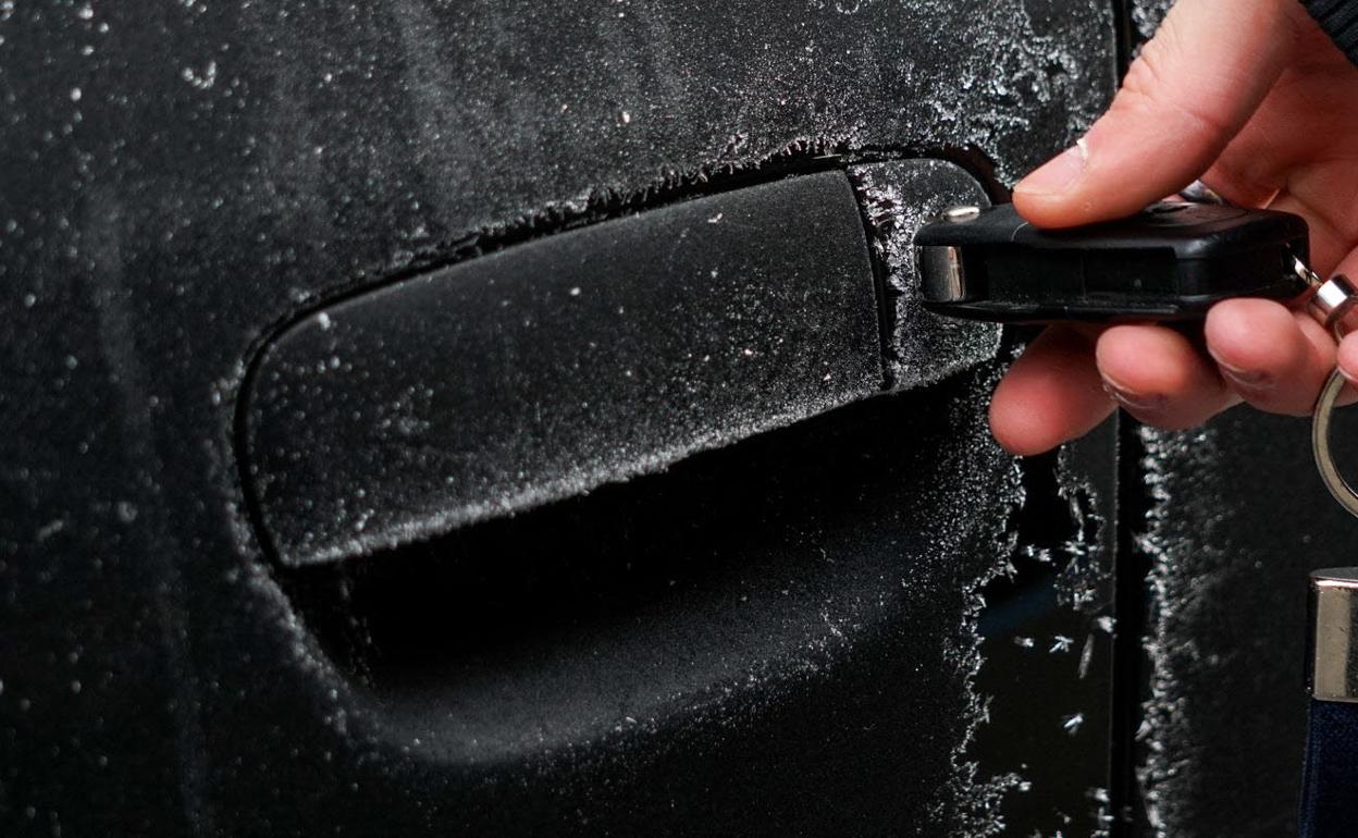 Imagen de archivo de una persona intentando abrir la puerta de su coche cubierto de hielo.