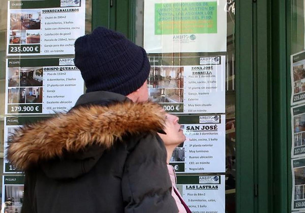 Una pareja mira el escaparate de una oficina inmobiliaria.