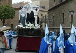 Un herrmano cubre las imágenes de un paso para protegerlas de la lluvia en una procesión en Salamanca.
