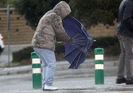 Un hombre trata de cerrar el paraguas pese al viento.