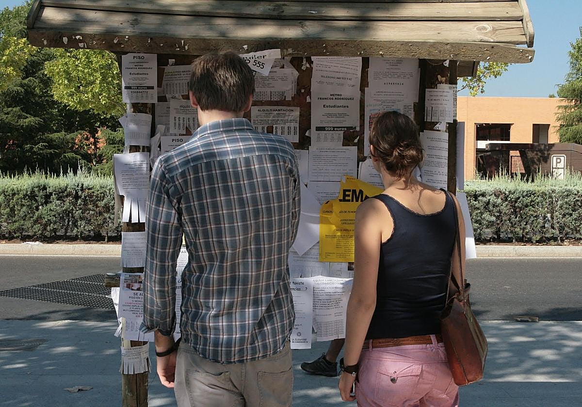 Dos personas observan anuncios de pisos y habitaciones de alquiler.
