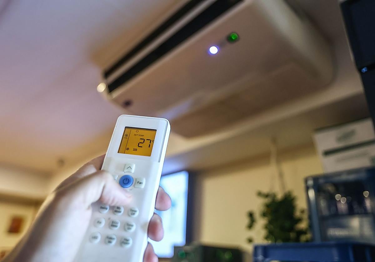 Una persona manipula el mando de un sistema de aire acondicionado.