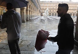 Dos personas pasean con paraguas por la Plaza Mayor de Salamanca.