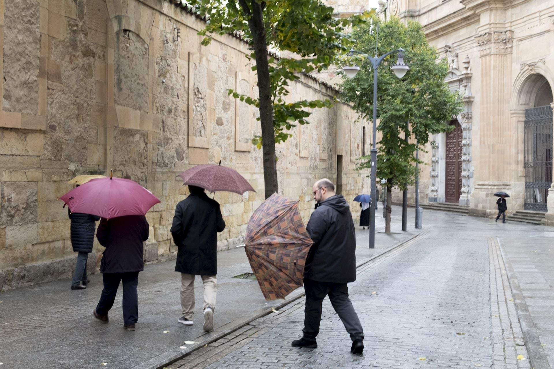 Viandantes se protegen del viento y la lluvia en Salamanca.