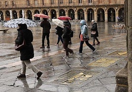 Varias personas pasean con paraguas por la Plaza Mayor de Salamanca.
