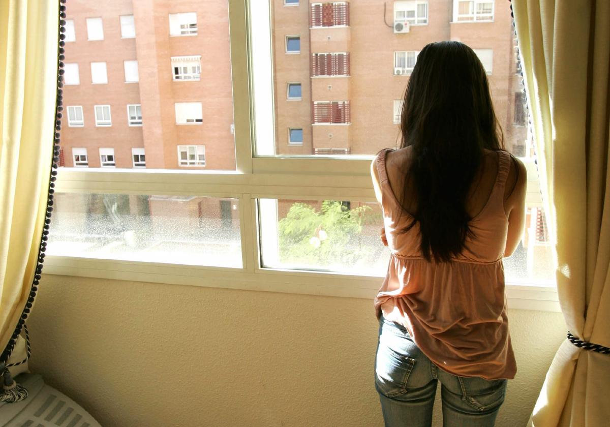 Una mujer observa por la ventana en un piso en una imagen de archivo.