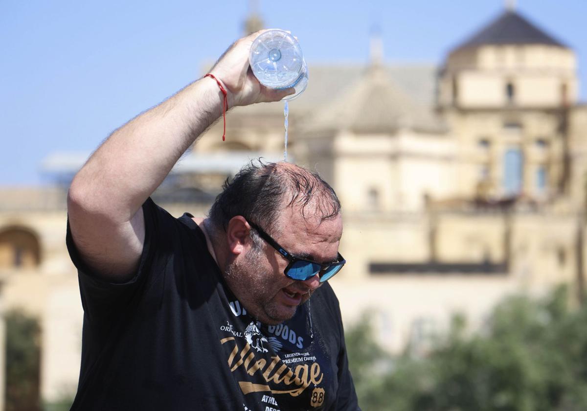 Un hombre trata de refrescarse echándose agua de una botella en la cabeza.