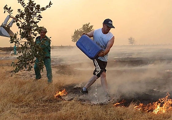 Dos personas se esfuerzan en apagar el fuego de Cipérez este viernes.