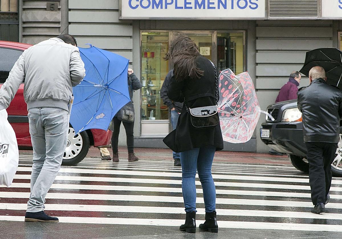 Varias personas cruzan por un paso de peatones en un día de viento y lluvia en Salamanca.