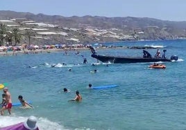 Migranten gehen am helllichten Tag am Strand von Castell de Ferro an Land, der voller Badegäste ist