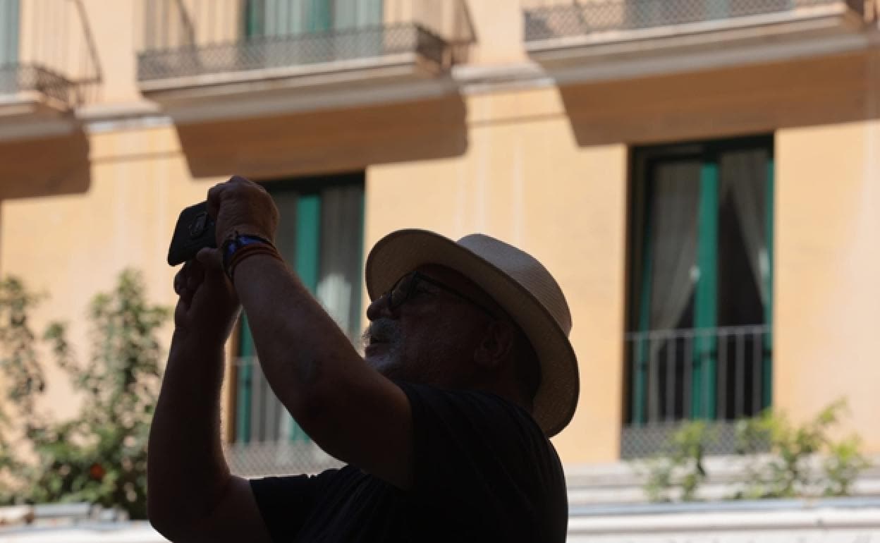 A tourist, protected from the sun with a hat, takes a photo in Malaga city centre.