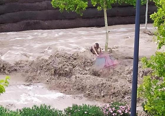 A woman clings to the roof of her vehicle to avoid being swept away by the flood.