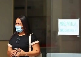 A woman at a hospital entrance wearing a mask, with the sign indicating that the wearing of a facemask is compulsory.