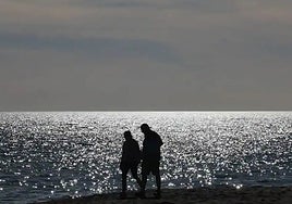 Two people stroll along Guadalmar beach in Malaga