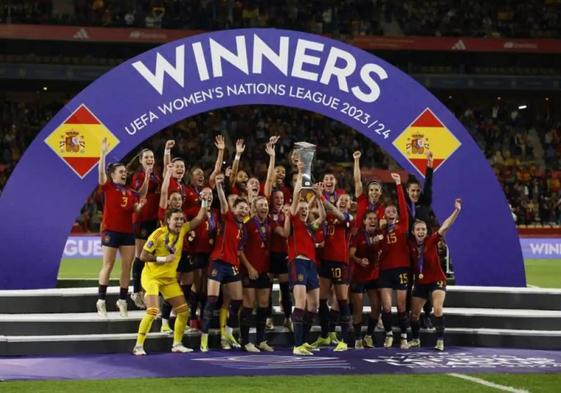 Spain's Irene Paredes lifts the Nations League trophy, surrounded by her teammates.