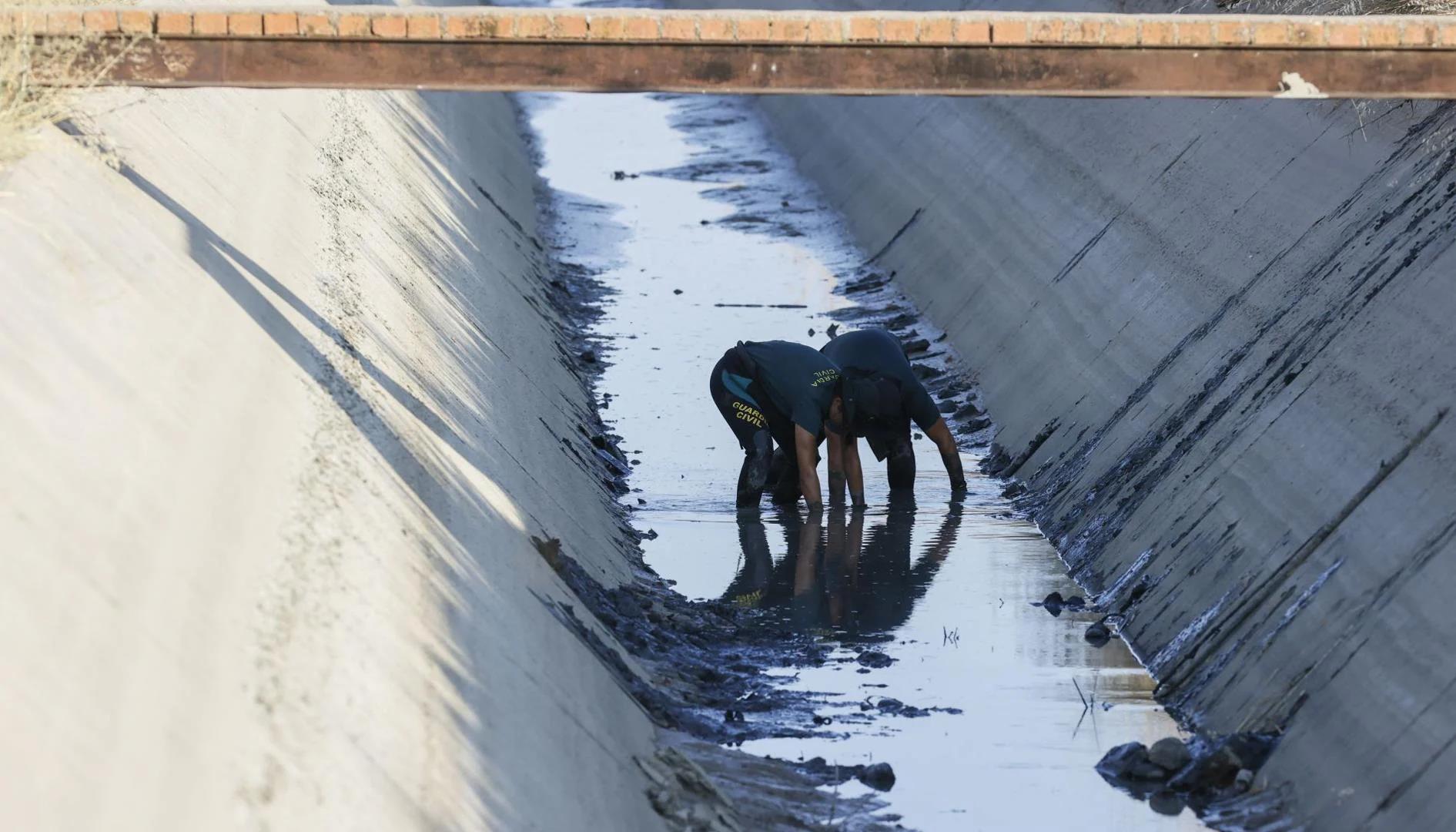Police officers search for the weapon in a drainage channel.